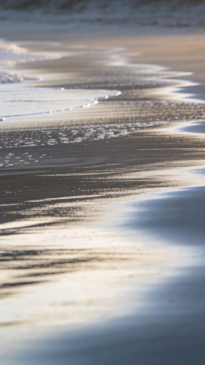 Vertical video: Thin surf band lapping shoreline, driven by swell, leaving foam and wet sand