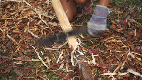 close up of woman wearing gloves shaving bark off large stick with machete