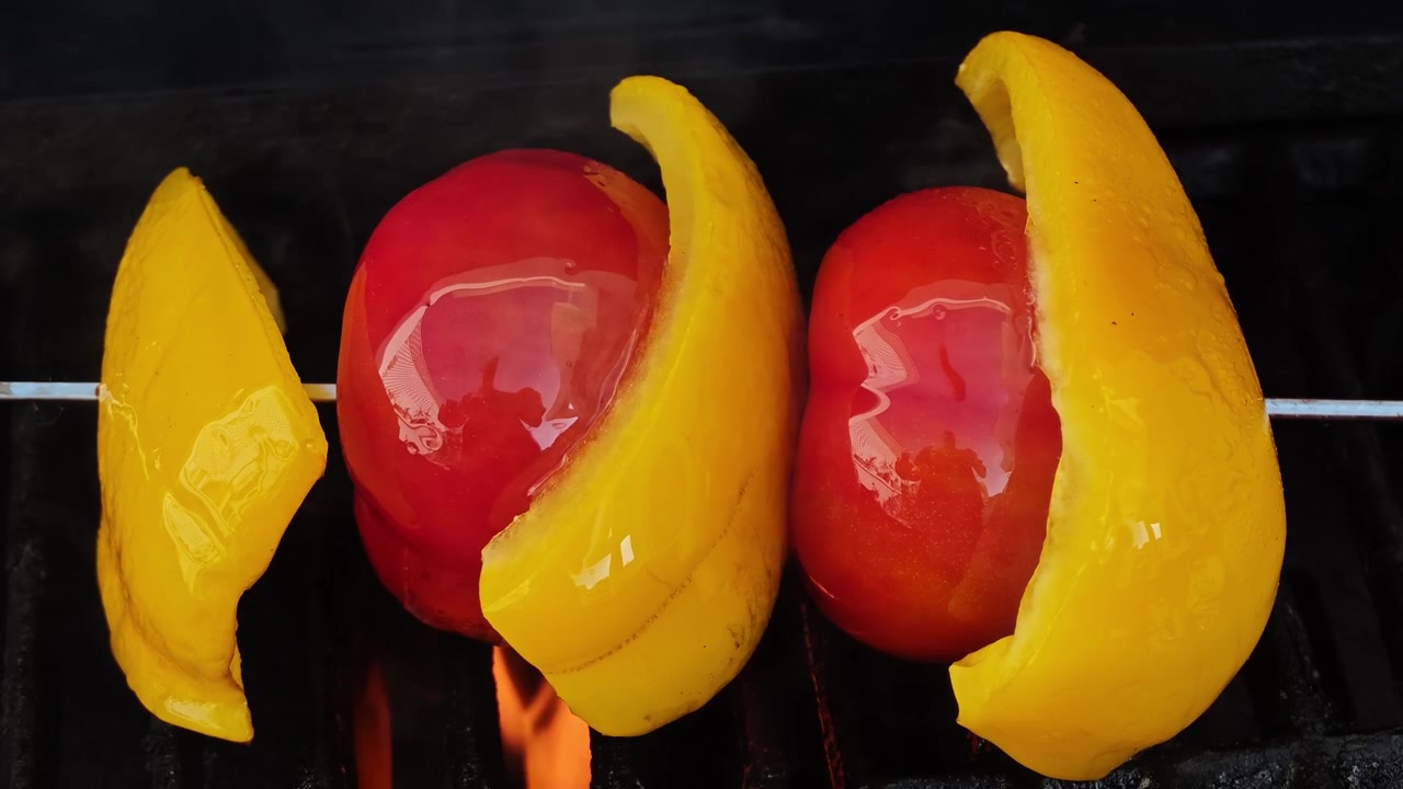 Primo piano al rallentatore di spiedino di verdure grigliate con pomodori rossi interi, fette di peperone giallo e olio d'oliva che schizza su una griglia BBQ nera, riprese macro cinematografiche dall'alto di cibo in 4K al tramonto!