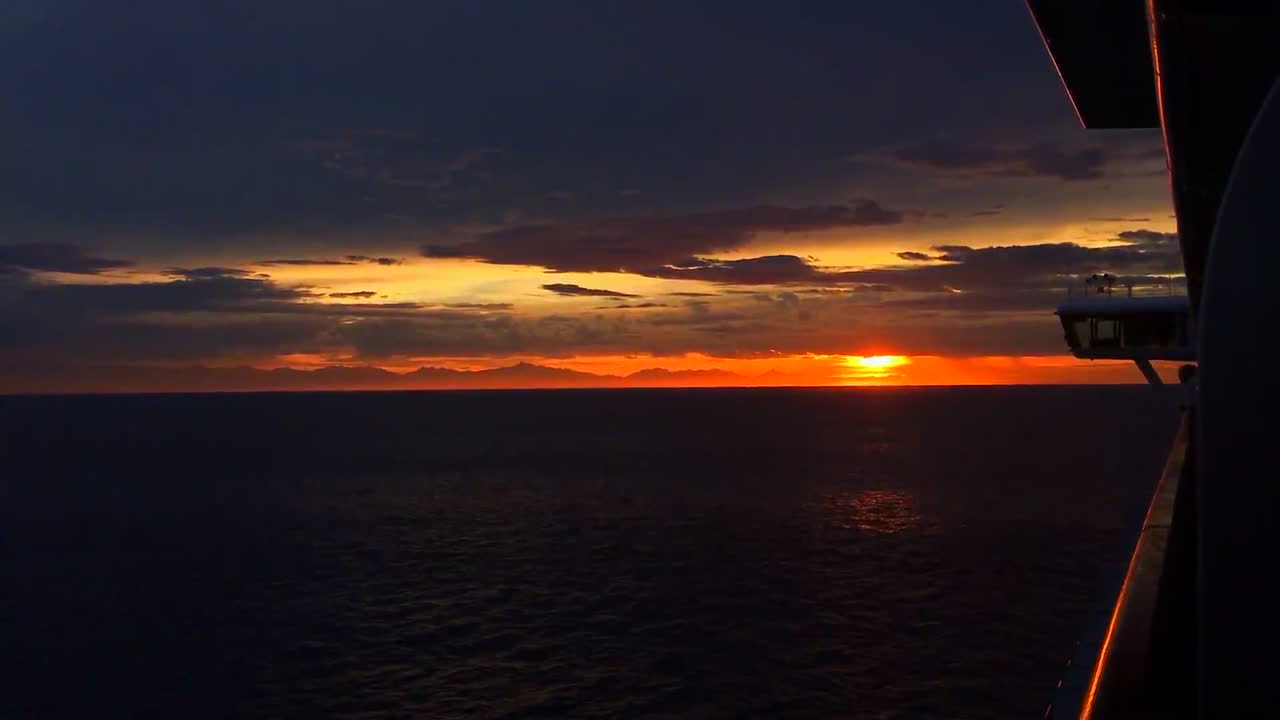 On a cruise with a amazing sunset, and you can see the land in the distance.