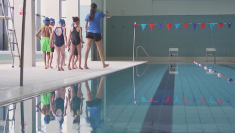 female coach walks children in swimming class along edge of indoor pool