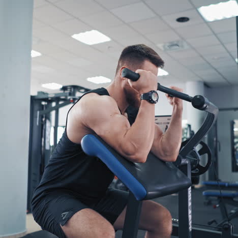 bearded man pumping his arm muscles in the gym. athletic bodybuilder training his biceps on a modern simulator and looking confidently forward.