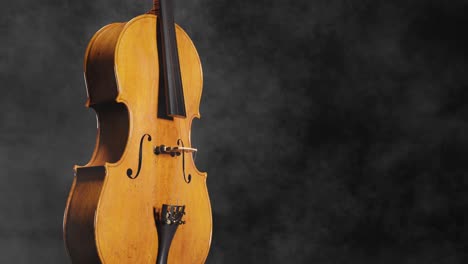 Smoke-blows-past-beautiful-wooden-cello-with-shining-face-on-black-background