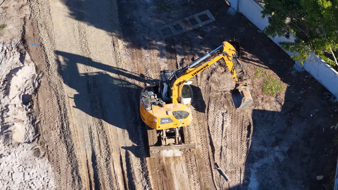 Aerial view of yellow excavator leveling soil at construction site in bright daylight