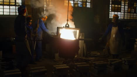 group of workers carrying container of molted metal at workshop 4k