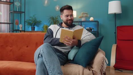 Young-man-relaxing-interesting-book-turning-pages-smiling-enjoying-literature-taking-a-rest-on-sofa