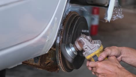 Hands-holding-a-grinder-moving-it-up-and-down-cleaning-the-left-side-of-the-wheel-hub-from-the-rust,-automotive-shop,-Thailand