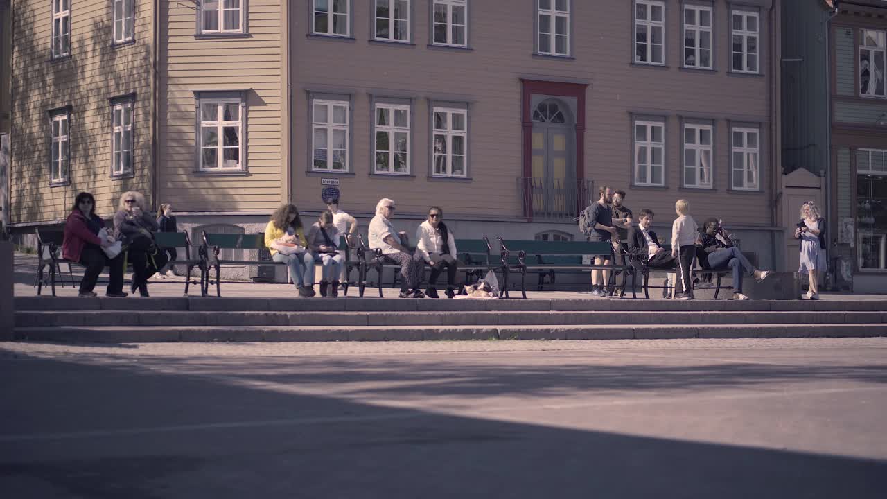 Norwegian People Sitting And Relaxing On Benches Along The Street In Tromso, Norway On A Sunny Morning. wide shot
