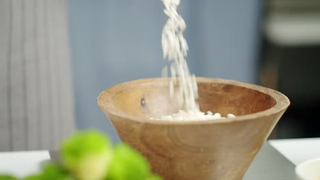 crop woman pouring dry rice in bowl for cooking risotto