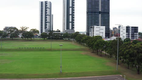 Aerial-drone-shot-flying-ascending-over-netball-courts-to-reveal-high-rise-structures-in-Liverpool,-Sydney-Australia