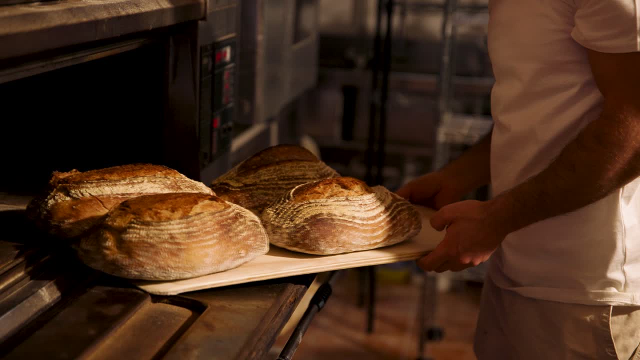 Bager tager friskbagt surdejsbrød ud af en varm ovn
