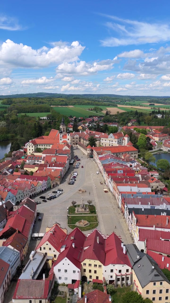 Dronekuva historiallisesta määriläisestä kaupungista, jossa on kaksi lampea, pitkä pääaukio ja renessanssilinna, jota ympäröivät vihreä maaseutu ja kevätpellot, Telč, Tšekin tasavalta.