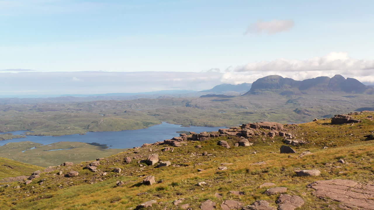스코틀랜드 북서쪽 고지대에 있는 stac pollaidh의 시네마틱 드론 샷, 바위산 꼭대기를 지나 수역을 드러내다