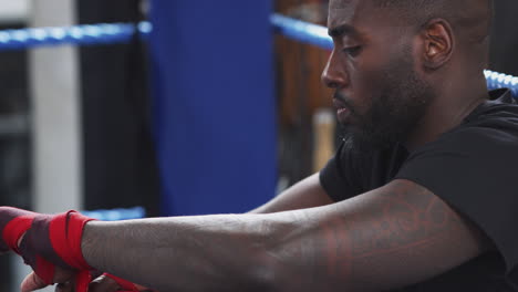 Male-Boxer-Training-In-Gym-Putting-Wraps-On-Hands-Sitting-In-Boxing-Ring