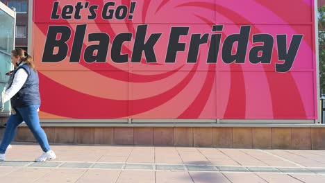 slow-motion footage of a woman strolling past a banner advertising the upcoming black friday sale and early holiday shopping deals in madrid, spain.