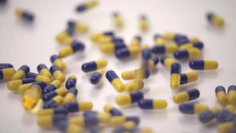 slow motion macro of blue and yellow pills dropped onto one yellow pill on white background