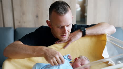 caucasian dad sits near the crib of his newborn. father caresses his child stroking the child.