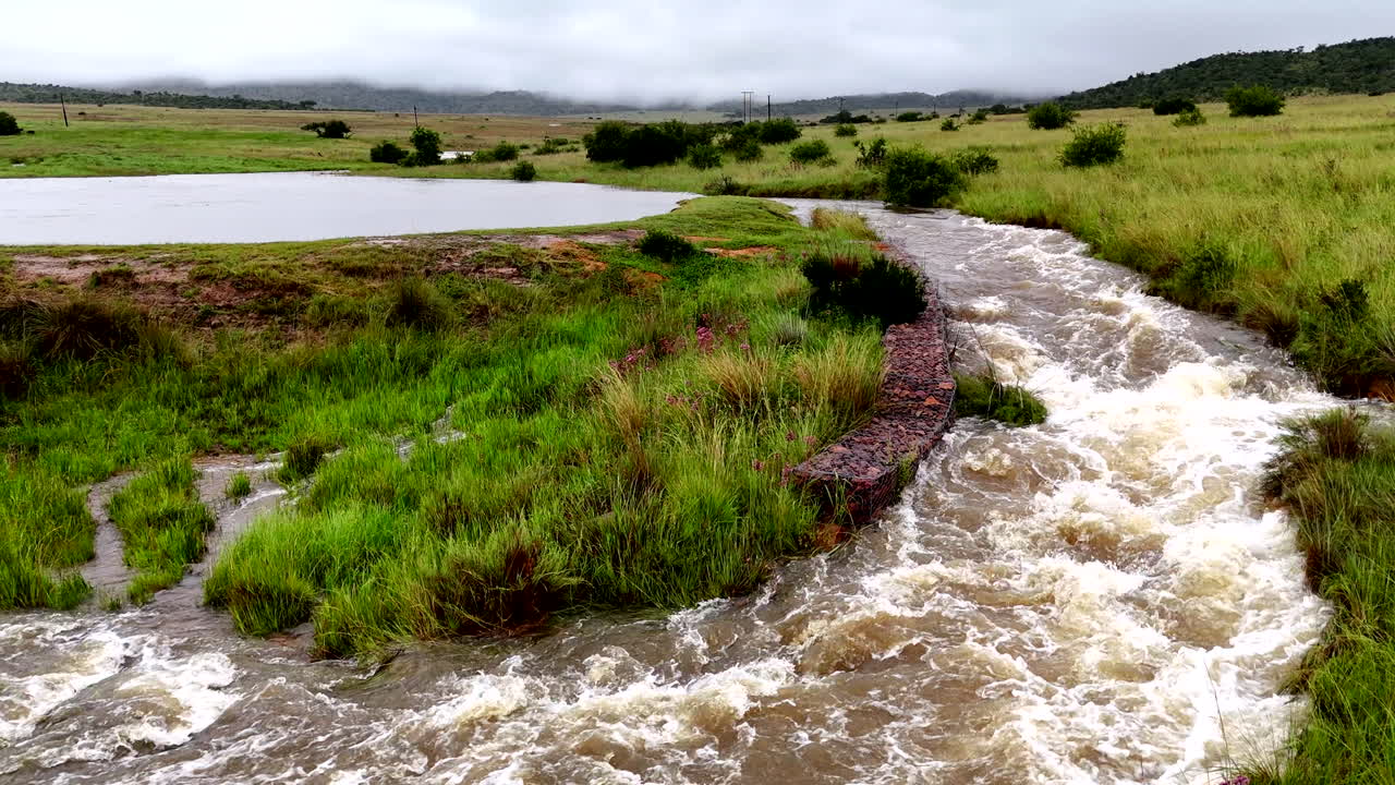 Flooded river flowing rapidly, with grassy banks and a wide landscape