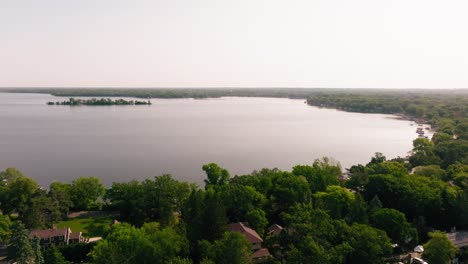 Drone-shot-of-large-lake-on-calm-summer-day,-featuring-a-wooded-island-in-the-middle-of-the-water