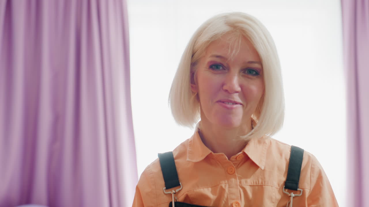 Florist wearing black apron and orange shirt stands smiling in workshop near bouquet of dried roses, hydrangeas, and decorative flowers showcasing floral craft, creativity, and artisan skills