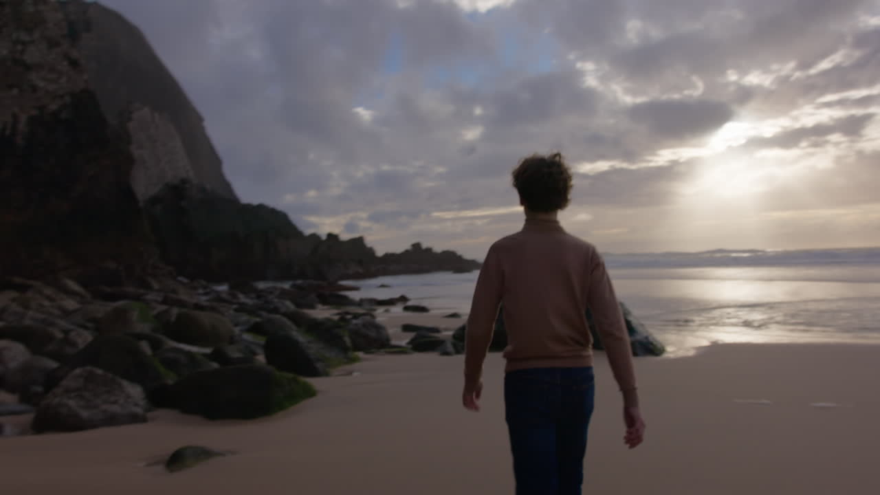 바위 해변 에서 일몰 을 상 하는 소년