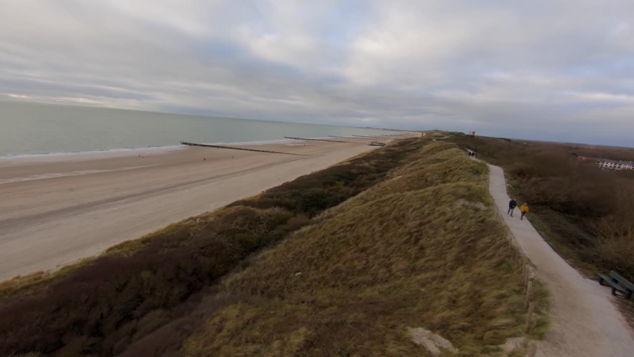 Soaring fast above the sand dunes and beach during an overcast winter day