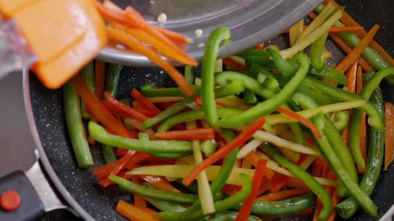 Tilføjer julienne-skårne røde, grønne og gule peberfrugter til non-stick panden til en wokret.