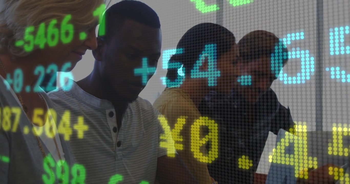 Fourth person leaning in with tablet, causing team typing on PCs and viewing finance ticker overlay