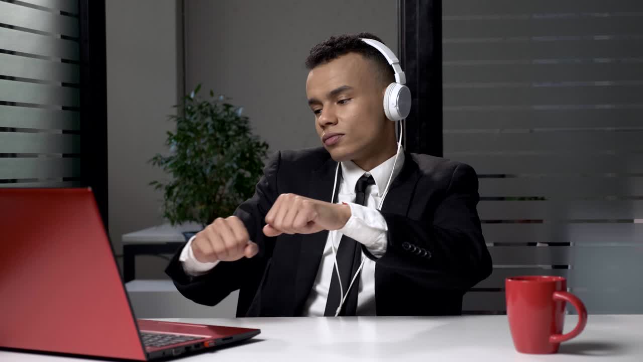 Young successful African businessman in suit listening to music on the computer in headphones, dancing in the office. 60 fps