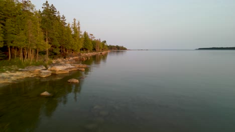 Aerial-fly-down-forested-lake-coastline,-Lake-Huron,-Michigan