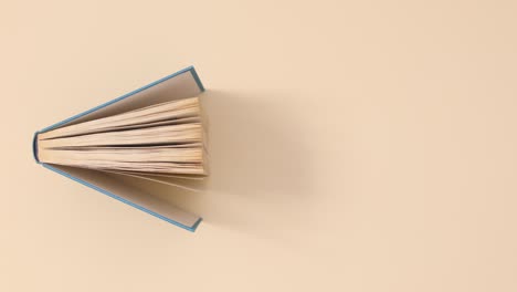 blue hardcover vintage book passing on beige background. stop motion flat lay