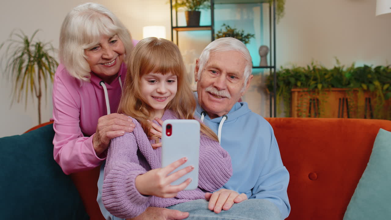 Grandfather grandmother and granddaughter child kid making video call online on smartphone at home