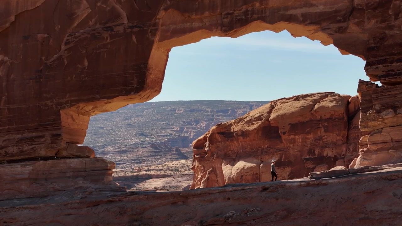 Ripresa da drone di una donna che cammina sotto un magnifico arco di arenaria nel paesaggio desertico dello Utah, USA