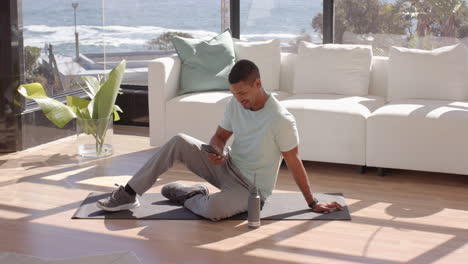 sitting on yoga mat, man using smartphone and relaxing in living room