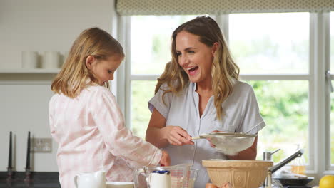 madre e hija con pijama horneando y haciendo panqueques en la cocina en casa juntos