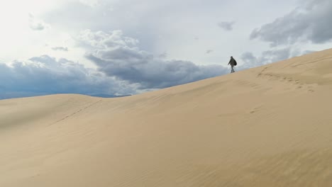 Zeitlupe-Einer-Dame-Mit-Rucksack,-Die-über-Den-Kamm-Einer-Hohen,-Fernen-Sanddüne-Läuft