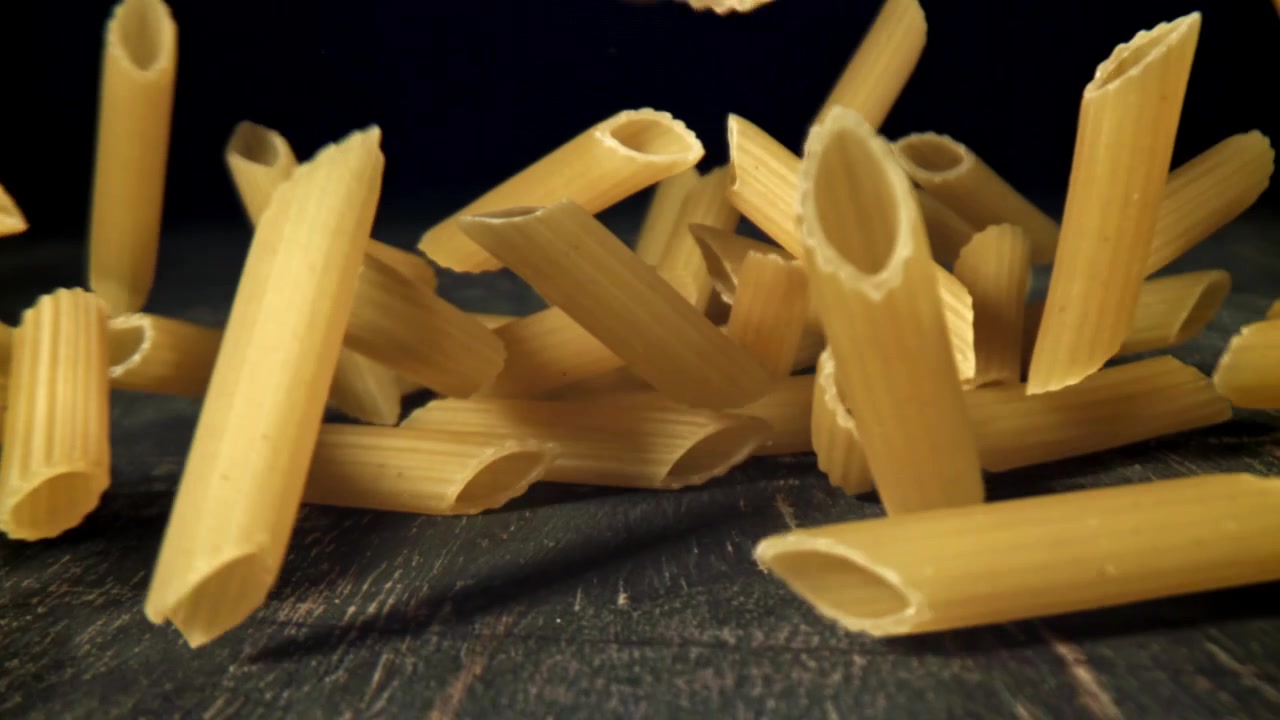 Penne-Nudeln fallen in Zeitlupe auf dunklem Hintergrund