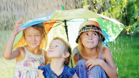 tres alegres niñas despreocupadas bajo el paraguas de los colores del arco iris hay una lluvia cálida feliz chi