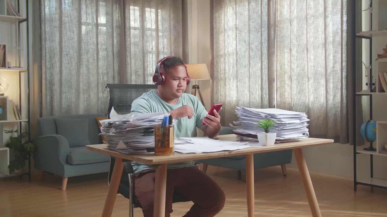 사무실 에서 문서 를 처리 한 후 에 헤드폰 을 착용 하고 스마트폰 에서 음악 을 듣고 있는 한 아시아인