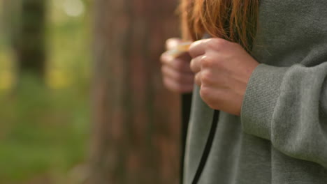 close-up of lady hiking through lush forest, gripping backpack straps with long, well-manicured nails, long hair flows over her shoulders wearing gray sweatshirt, against soft, blurred greenery