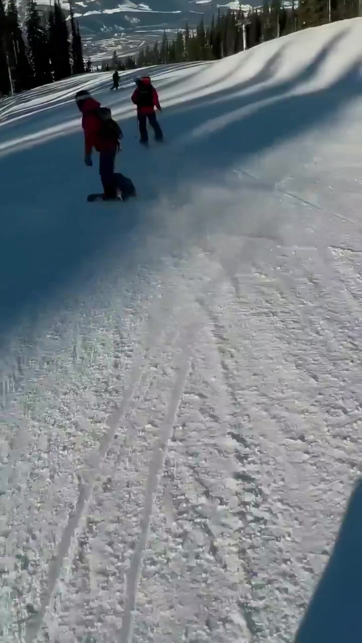 Video verticale: Telecamera che riprende uno snowboarder con giacca rossa che intaglia una pista a 'corduroy' verso la cresta, spazio per il testo.