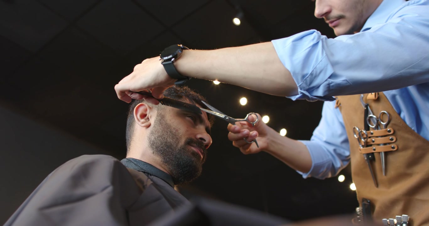 Barber trimmer kunde, løfter hår med kam og saks for at færdiggøre klipningen i salonen, med kopiplads