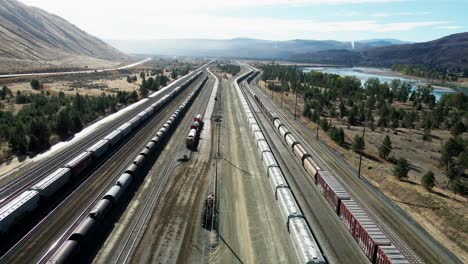 forward flight dolly drone shot flying over a railroad station in a desert environment on a sunny day next to a highway and a river and mountains in the background and powerines in the picture