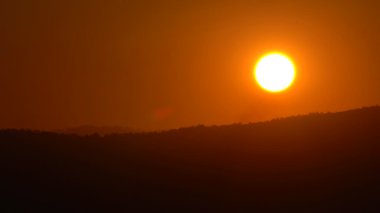 Solnedgang over himmel og skyer, smukt solskin og lysstråler over bakker eller bjerge på silhuetbaggrund.