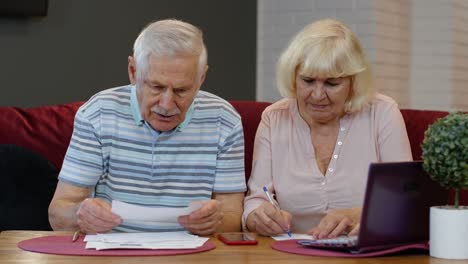 senior pensioner couple checking and calculating domestic bills bank loan payment doing paperwork