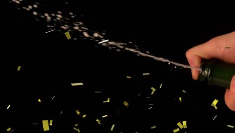 Golden-confetti-falling-over-mid-section-of-person-spraying-champagne-against-black-background