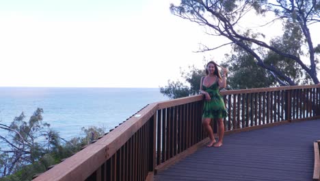 chica sexy arregla el cabello mientras se apoya en una valla de madera - vista al mar desde el mirador north gorge walk in point lookout, queensland, australia