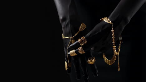ornate gold jewelry on dark hands against black background