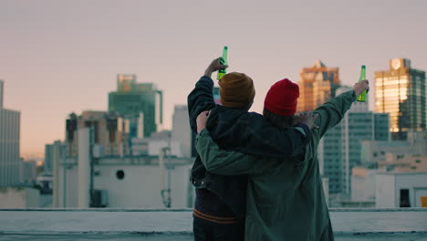 happy friends on rooftop with arms raised celebrating friendship enjoying hanging out together drinking alcohol embracing freedom looking at urban city skyline at sunset