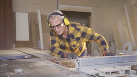 male carpenter working in carpentry factory cutting boards with saw.